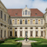 Außenansicht der Münchner Residenz: Barocke Fassade mit Säulenportikus und kupfergrünem Dachgiebel, davor gepflasterter Platz und historischer Laternenpfosten.