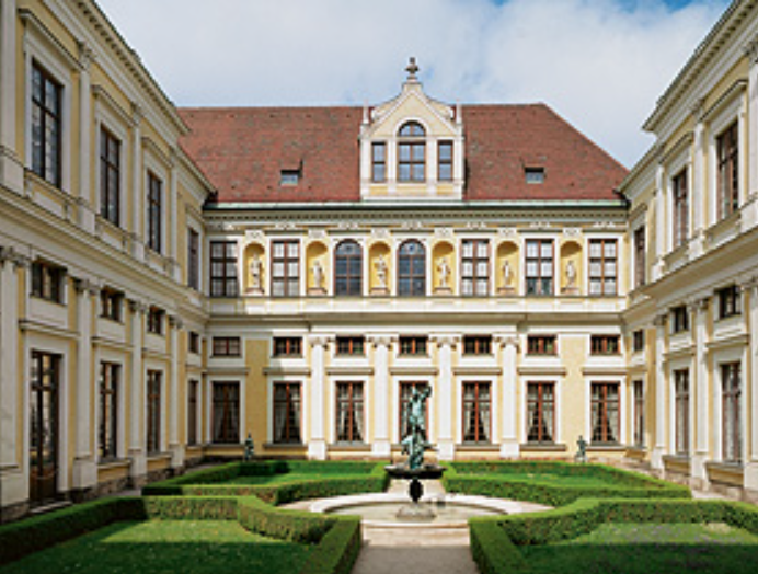 Außenansicht der Münchner Residenz: Barocke Fassade mit Säulenportikus und kupfergrünem Dachgiebel, davor gepflasterter Platz und historischer Laternenpfosten.